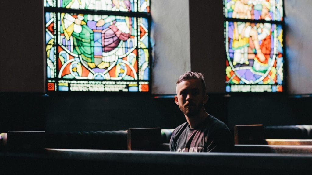 How does culture influence the church? / Photo: Man sitting in church with stained glass windows behind him.